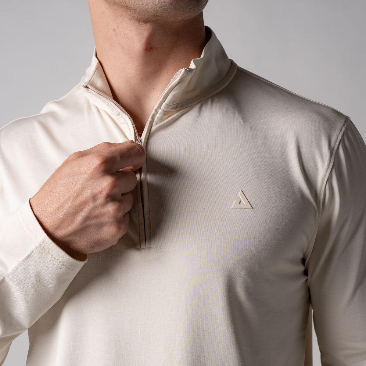 Mann zieht den Reißverschluss eines cremefarbenen, langärmligen Sportshirts mit Stehkragen hoch.