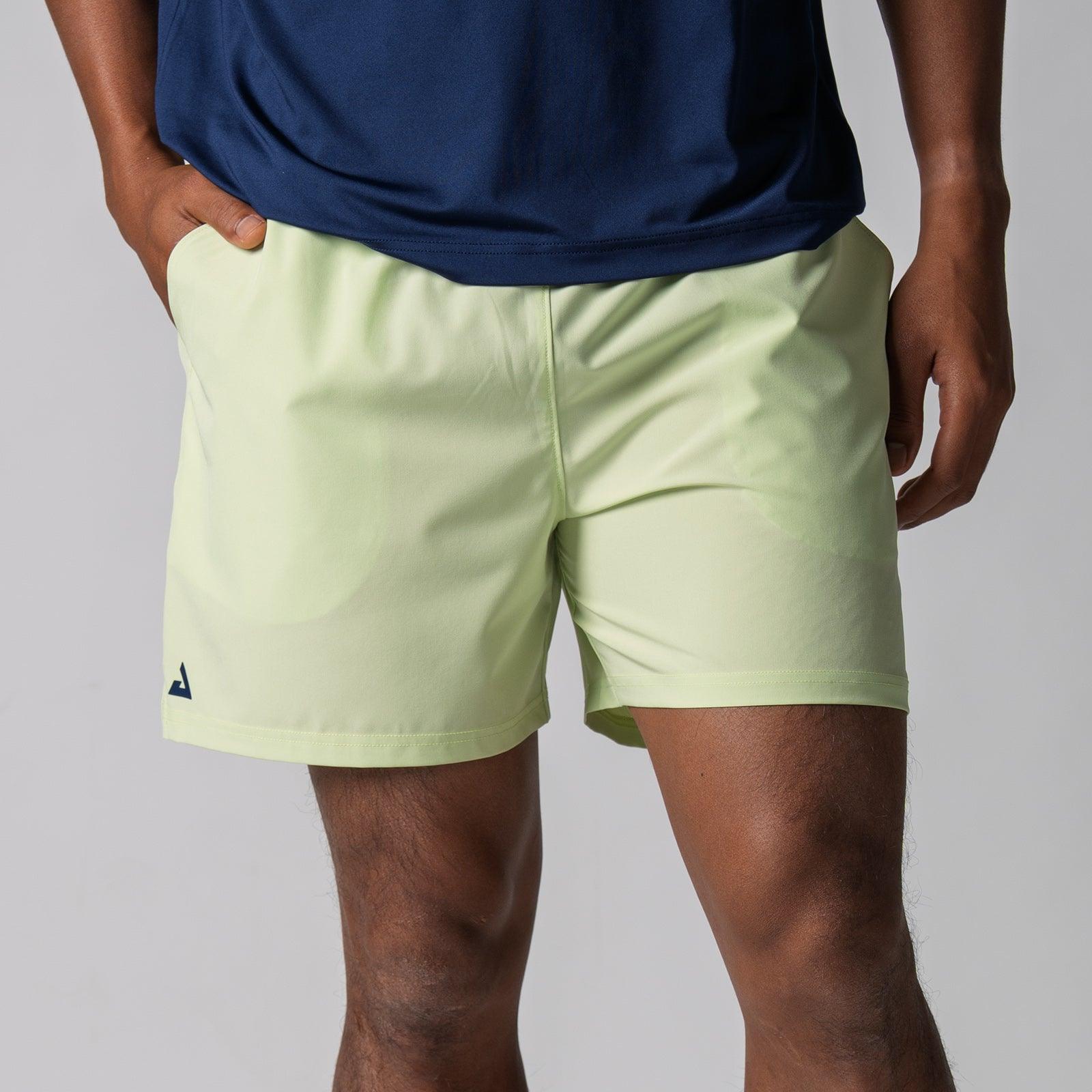 Männliche Person trägt hellgrüne Sportshorts mit Taschen und dunkelblauem Shirt.