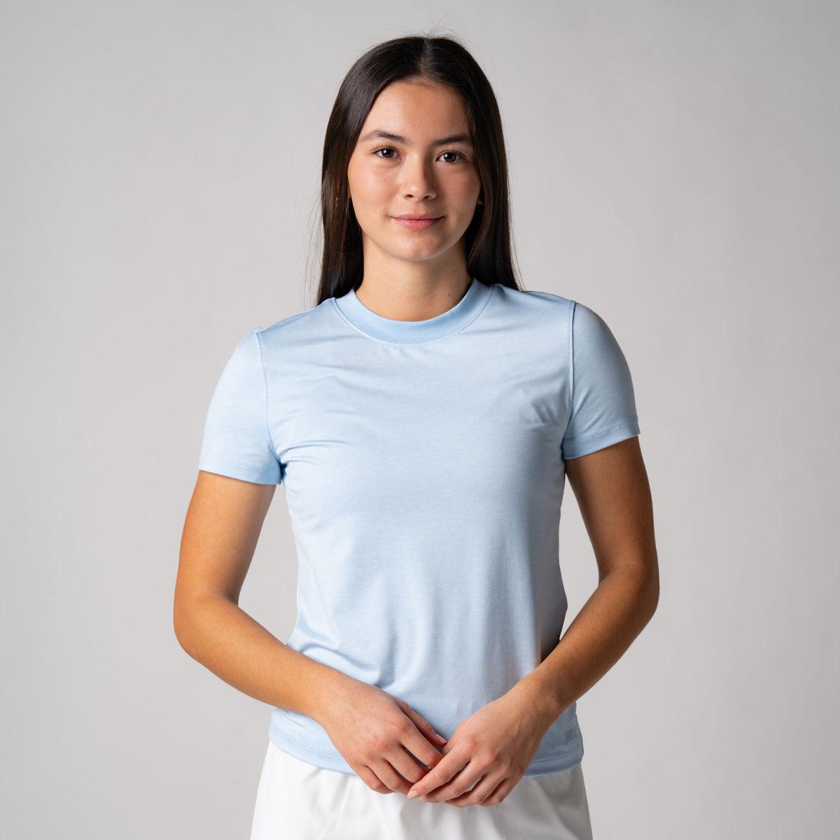 Frau trägt hellblaues, kurzärmeliges T-Shirt vor hellem Hintergrund.