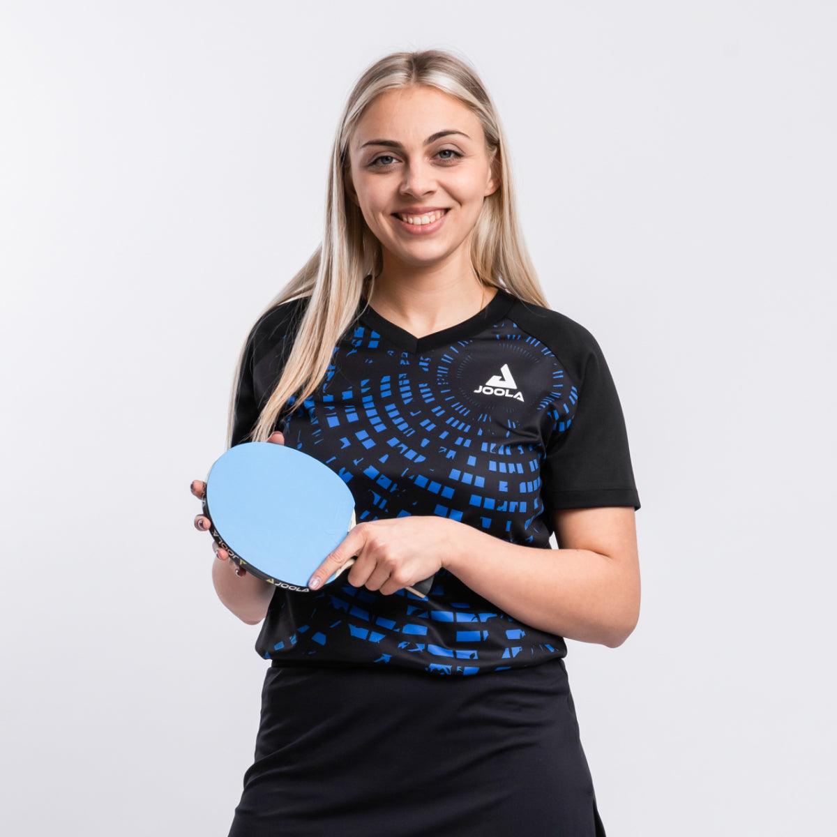 Frau in schwarzem und blauem JOOLA Tischtennis-Trikot hält blauen Tischtennisschläger.