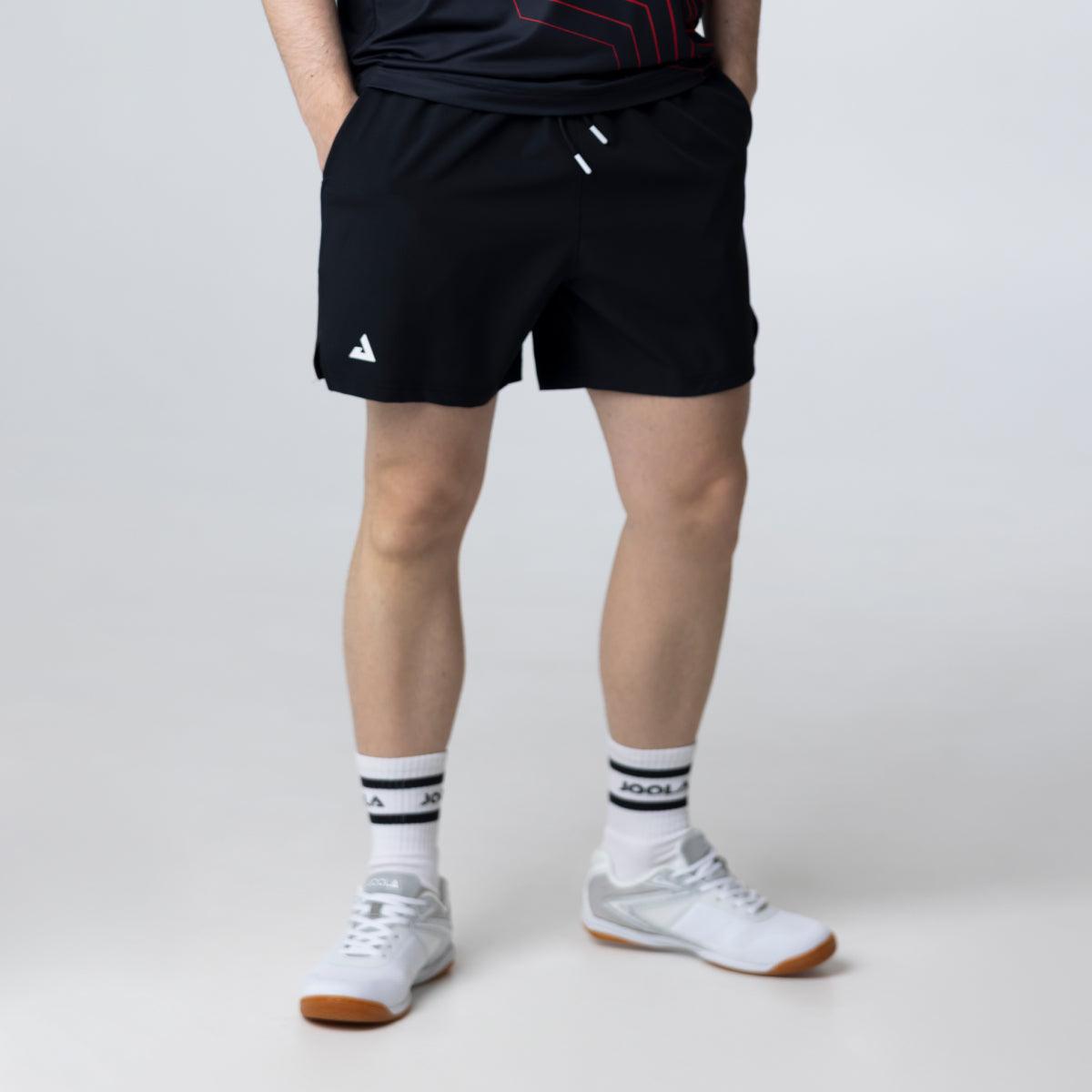 Mann trägt schwarze Sportshorts mit weißem Logo, weiße Sportsocken und weiße Sportschuhe.