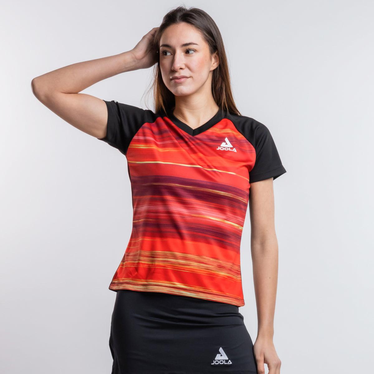 Frau trägt rotes JOOLA Sportshirt mit schwarzen Ärmeln und schwarzem JOOLA Rock vor weißem Hintergrund.