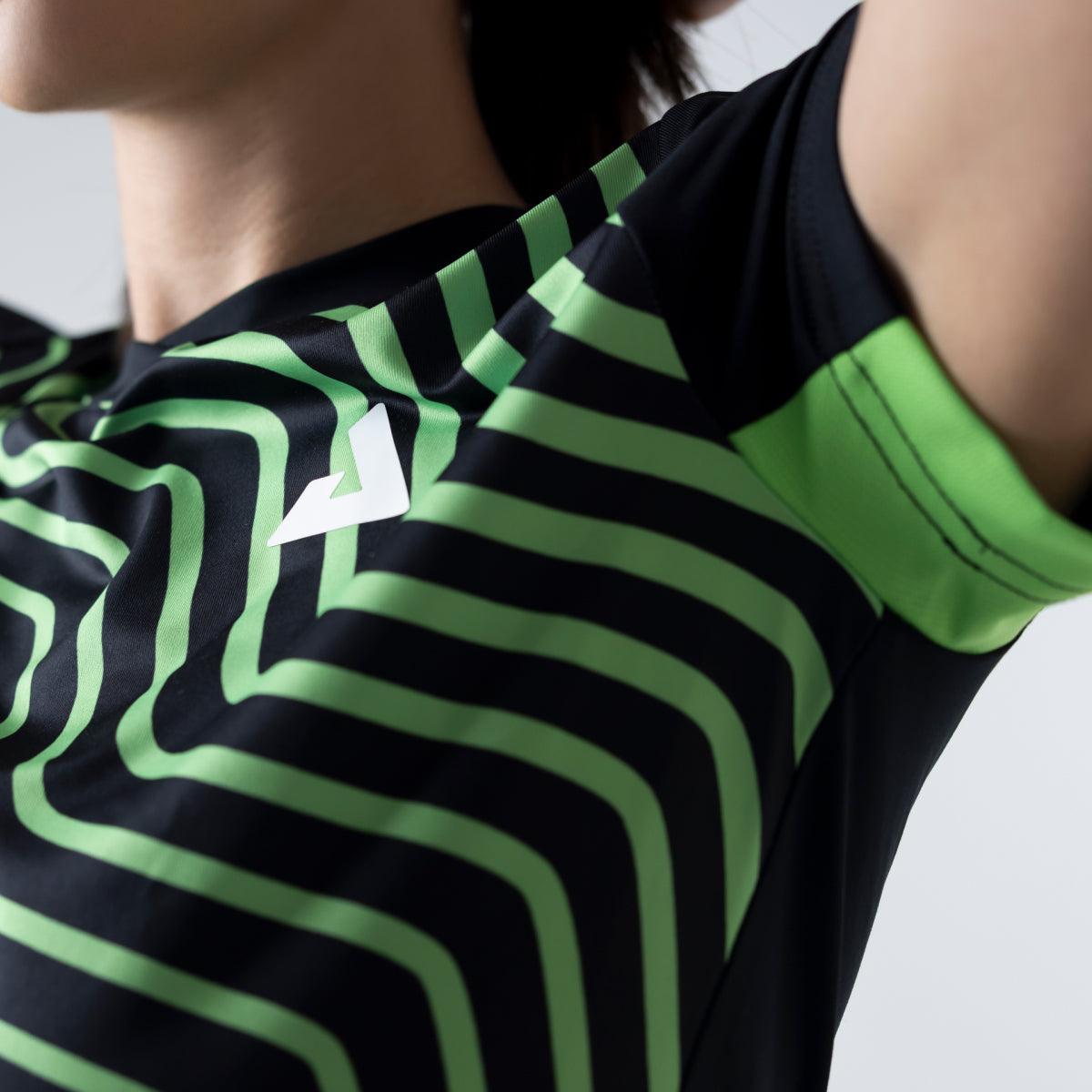 Frau trägt ein eng anliegendes Sportshirt mit schwarz-grünem Streifenmuster und weißem Logo auf der Brust.