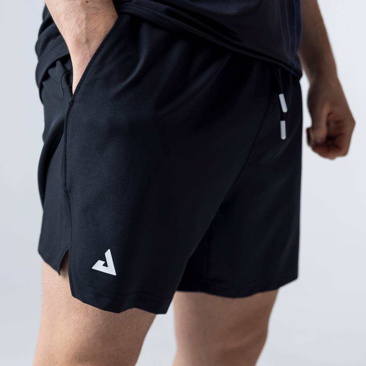 Mann trägt schwarze Sportshorts mit seitlicher Tasche und kleinem weißem Logo am Bein.