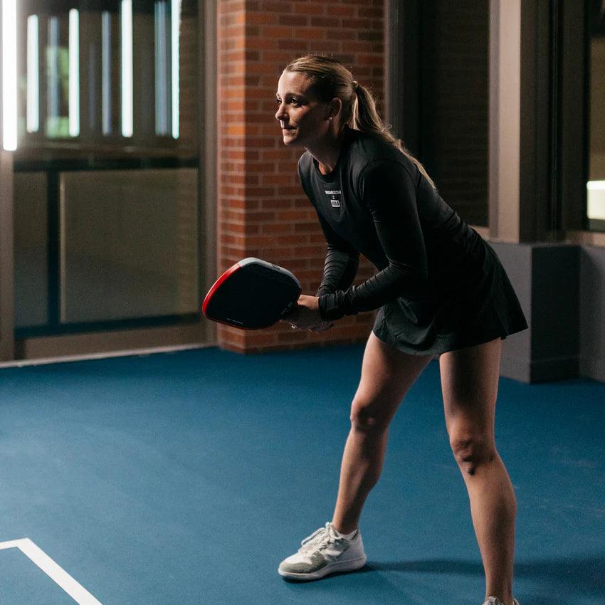 Frau in Sportkleidung hält einen Padel-Schläger auf einem Indoor-Padelplatz.